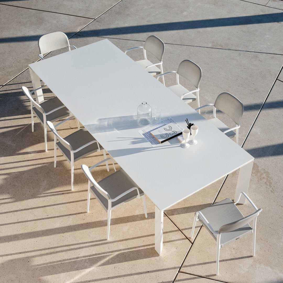 White rectangular dining table with eight matching chairs. Minimalist design with clean lines and a modern aesthetic.