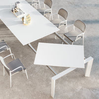 Modern white rectangular table with sleek design and gray patterned chairs, set on a minimalist concrete floor.