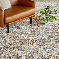 Brown and cream textured rug with subtle patterns, complementing a stylish brown leather chair and green plants.