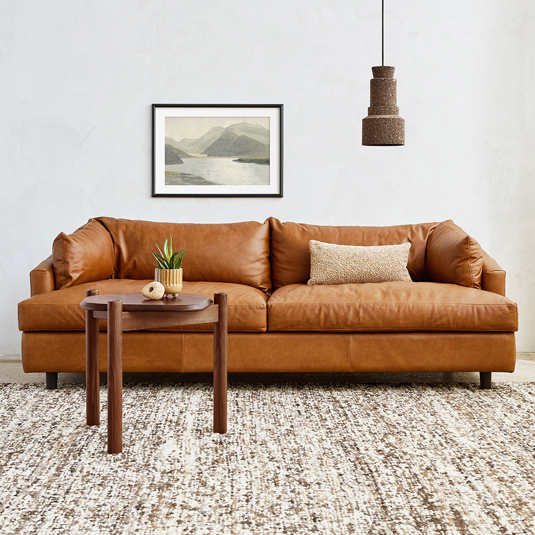 Brown leather sofa with textured pattern, natural wood side table, and neutral-toned area rug featuring subtle earthy shades.