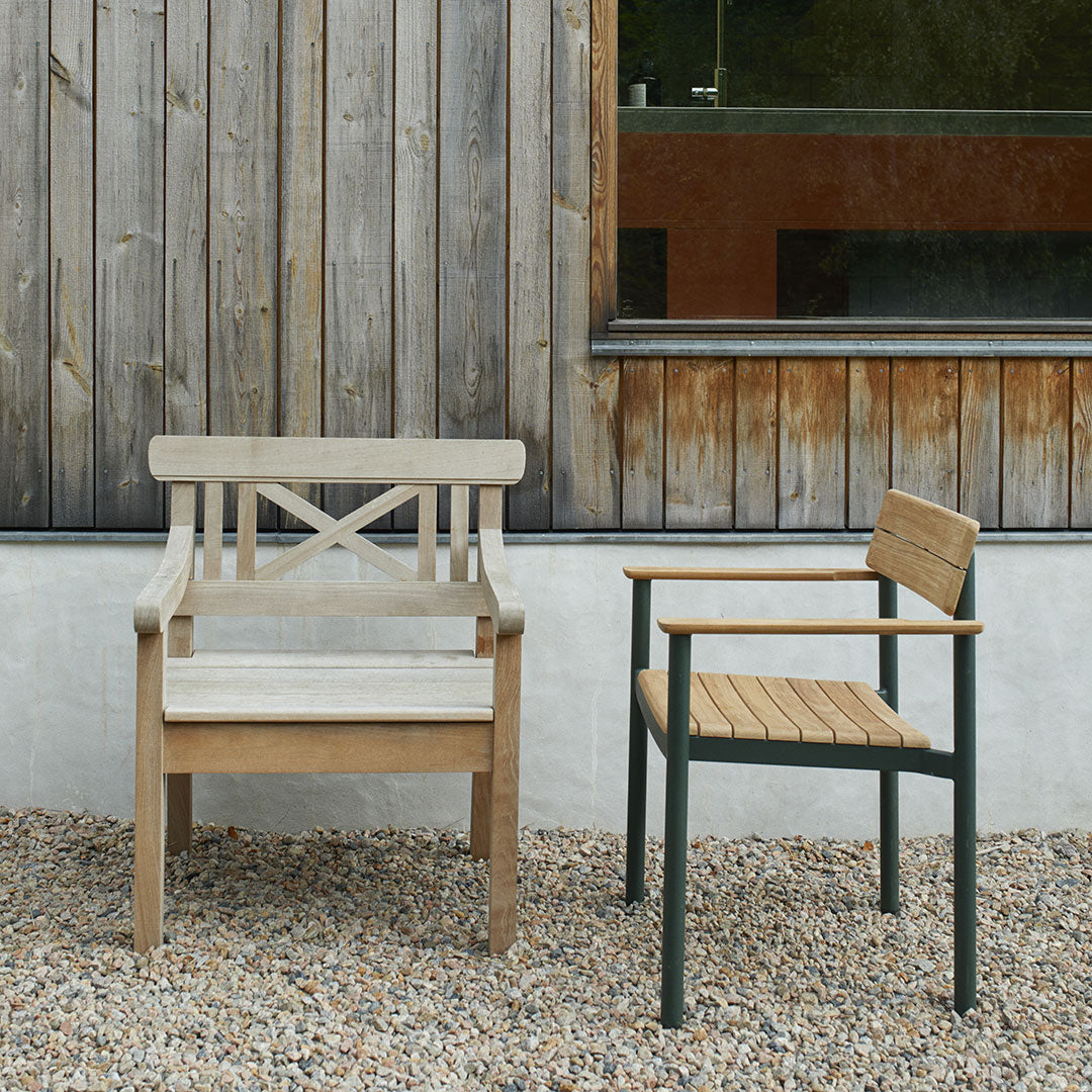 Two outdoor chairs: one in light wood with a cross-back design, and another in dark green metal with natural wood accents.
