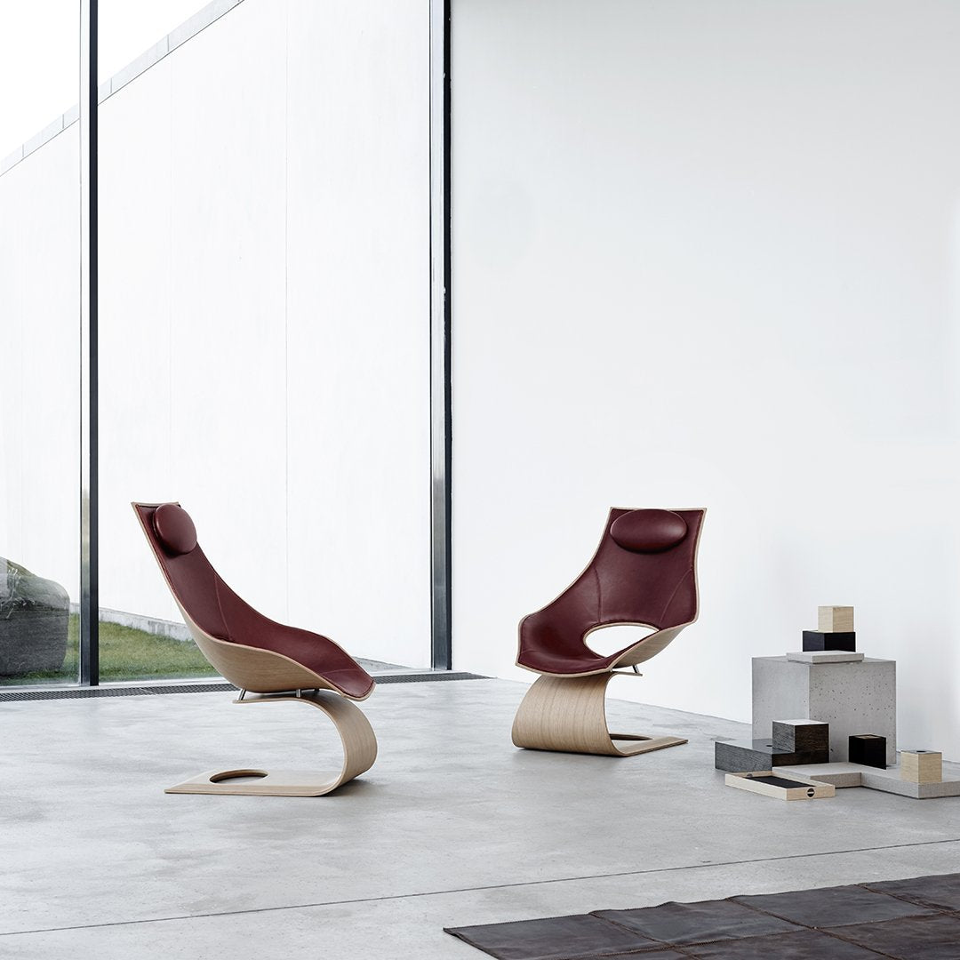 Modern rocking chairs with burgundy leather upholstery and curved wooden bases, showcased in a minimalist setting.