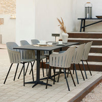 Stylish outdoor dining set featuring a sleek black table and modern gray chairs with vertical slats, set on textured stone pavers.