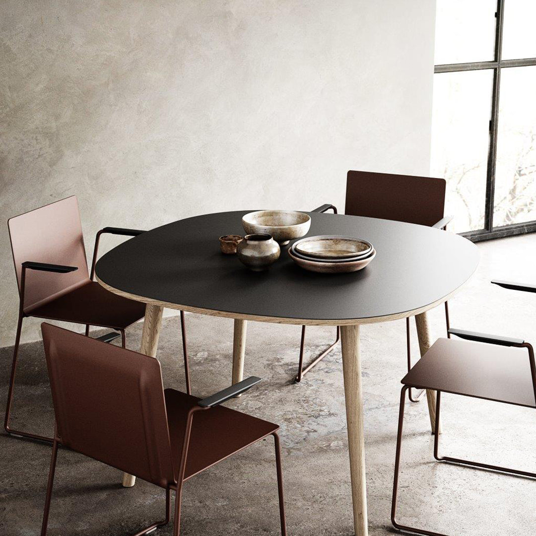 Modern round table with a sleek black top and light wood legs, surrounded by stylish brown metal chairs.