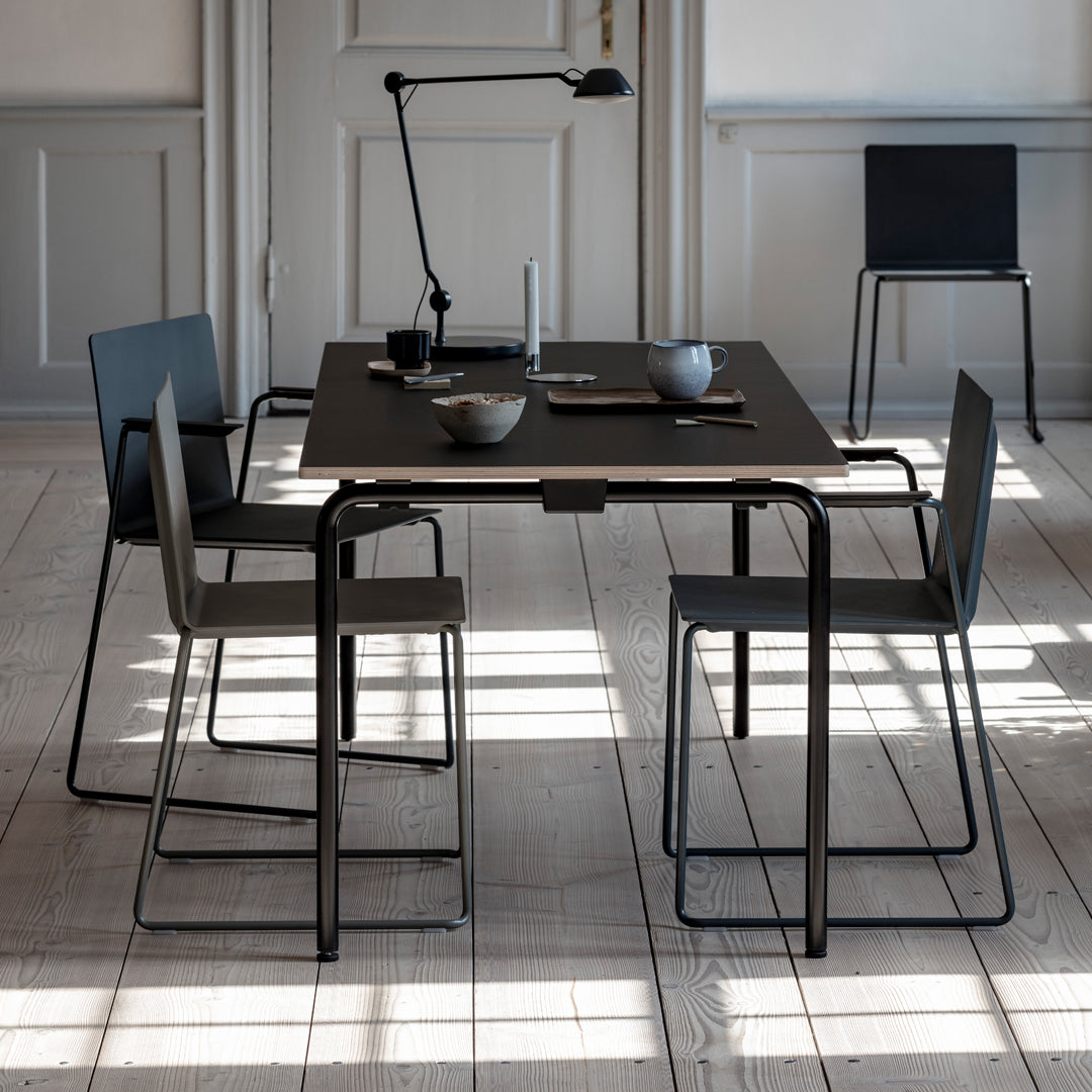 Black rectangular dining table with minimalist gray chairs, featuring sleek lines and a modern, neutral aesthetic.