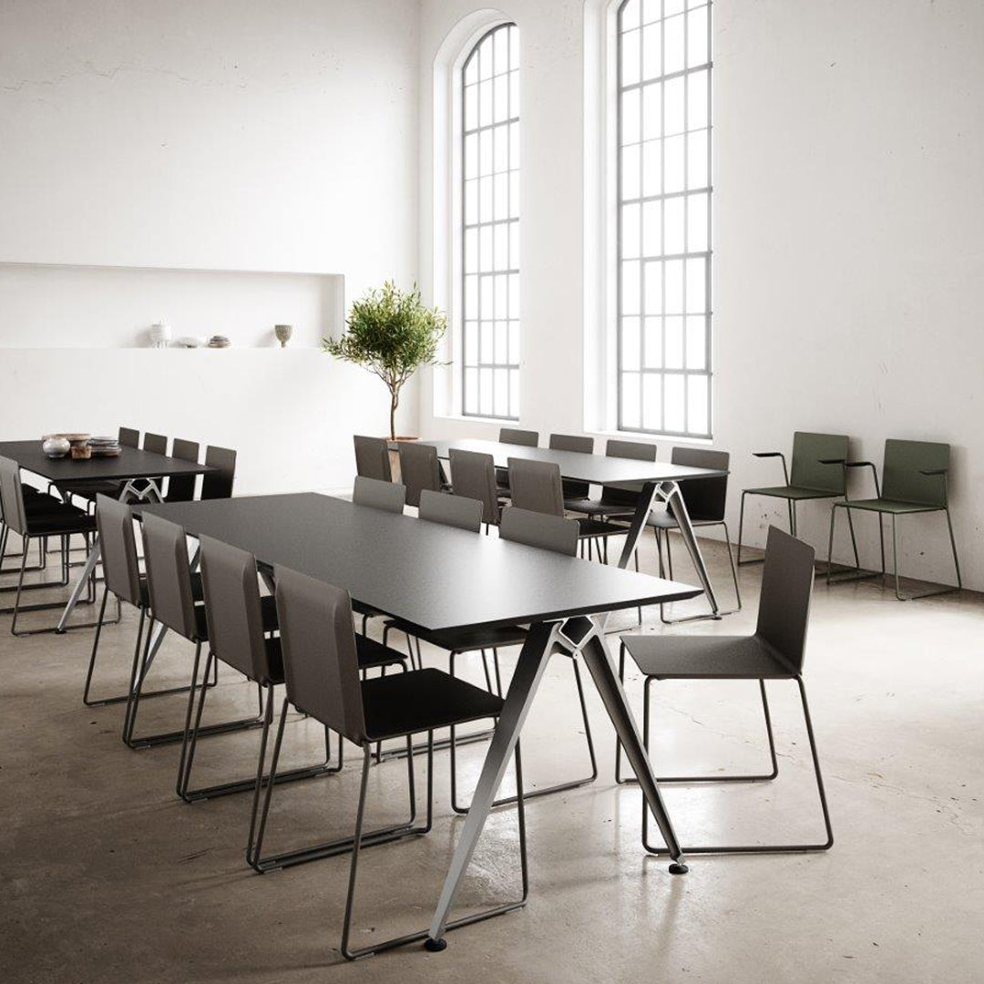 Modern black table with gray chairs in a minimalist room featuring large windows and concrete flooring.