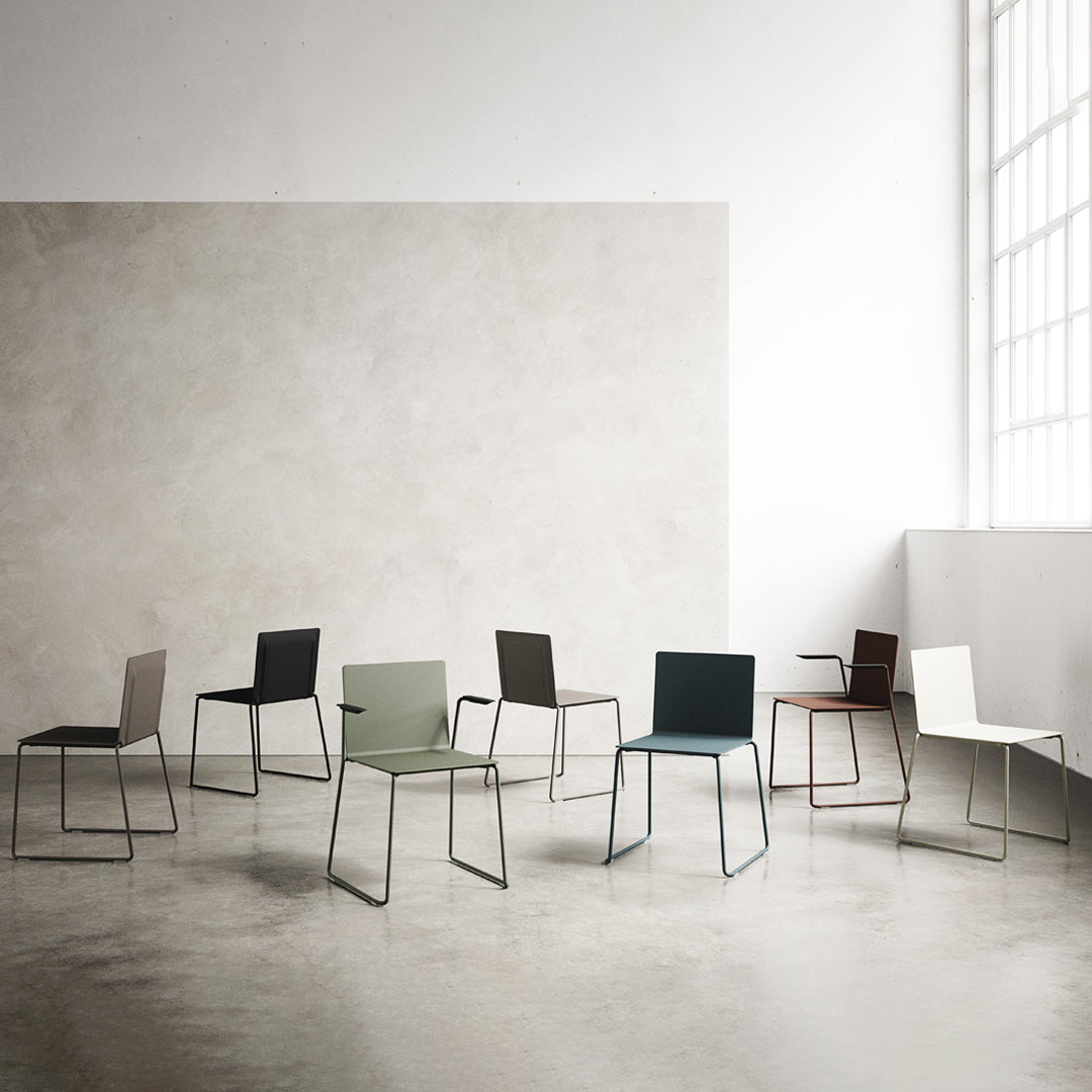 Modern chairs in a variety of muted colors: olive green, charcoal gray, navy blue, white, and maroon, on a minimalistic backdrop.