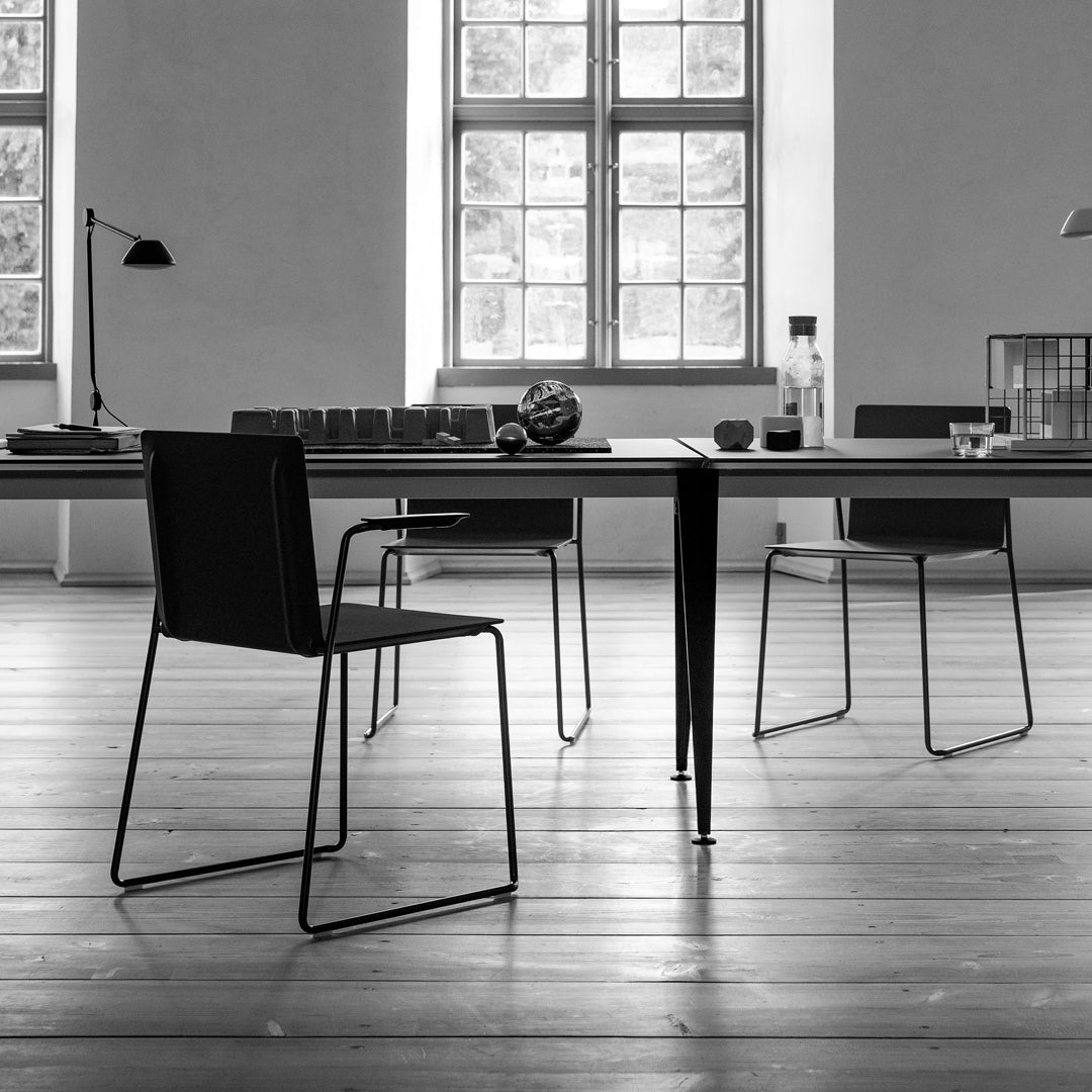 Sleek black chairs and a minimalist wooden table in a bright, neutral-toned room with large windows.