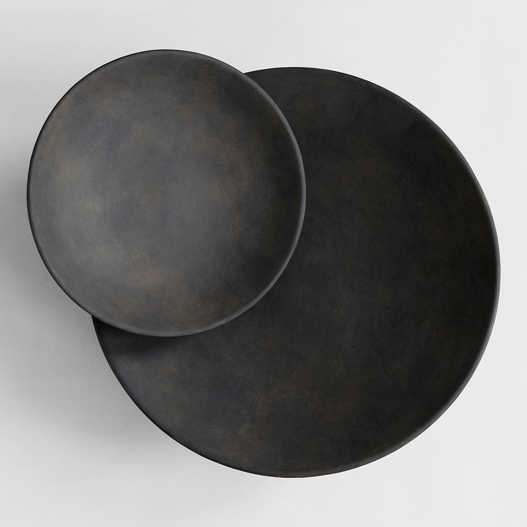 Two dark-toned textured ceramic plates, featuring a matte black finish with subtle brown undertones.