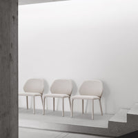 Set of three light beige chairs with a minimalist design against a white wall and concrete flooring.