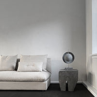 Soft beige sofa with textured cushions against a neutral gray wall, paired with a sleek circular table accent.