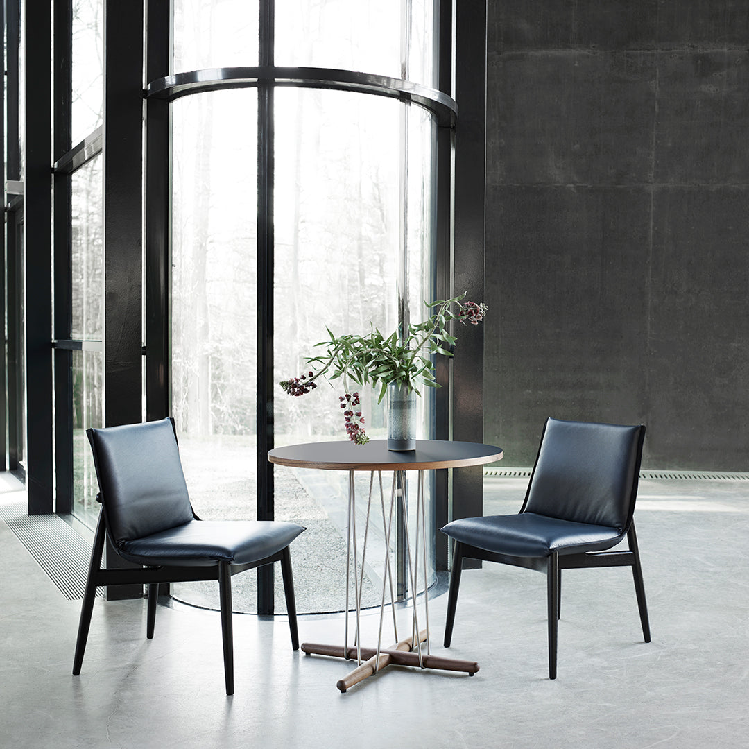 Modern black leather chairs with sleek lines and a round wooden table, set against a minimalist gray interior.