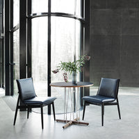 Modern black leather chairs with sleek lines and a round wooden table, set against a minimalist gray interior.