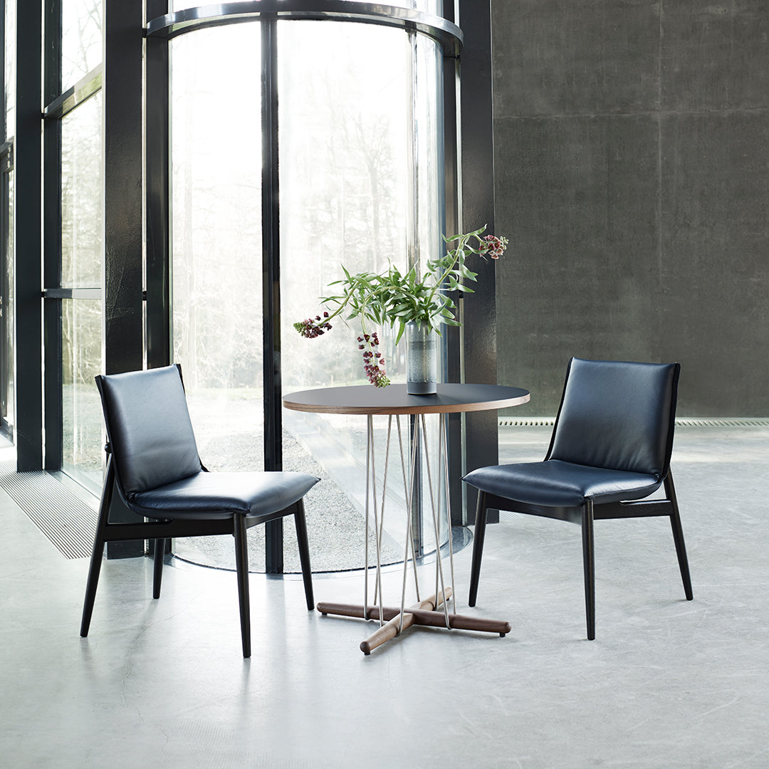 Modern black leather chairs with sleek lines around a round wooden table in a minimalist setting.