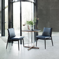 Modern black leather chairs with sleek lines around a round wooden table in a minimalist setting.