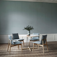 Light blue chairs with wooden legs around a round table, set against a muted teal wall and herringbone wood floor.