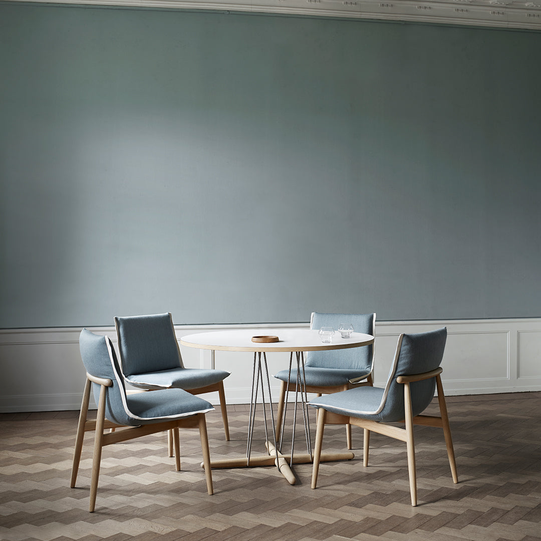 Light blue upholstered chairs around a round white tabletop, set on a patterned herringbone wooden floor.