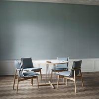 Light blue upholstered chairs around a round white tabletop, set on a patterned herringbone wooden floor.