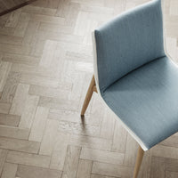 "Light blue upholstered chair on a textured herringbone wood floor, combining modern elegance with natural tones."