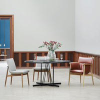 Modern dining setup with gray and white chairs, a black circular table, and a warm-toned leather accent chair.