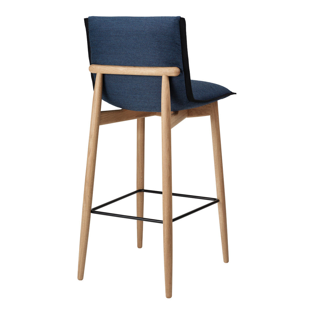 Blue upholstered bar stool with light wooden legs and a black metal footrest, featuring a minimalist design.