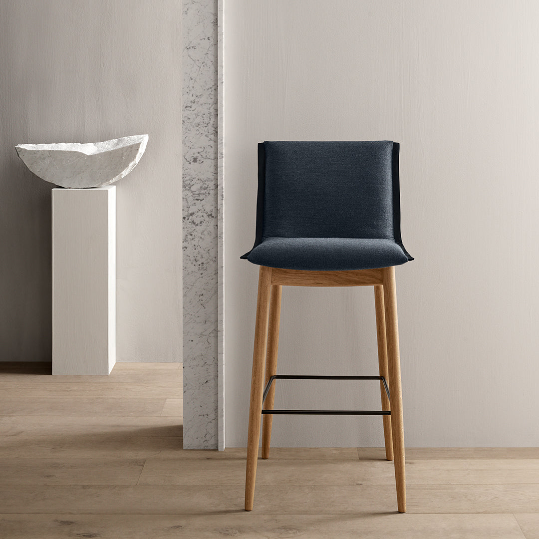 Modern dark blue upholstery on a wooden bar stool against a neutral background. Minimalist design and clean lines.