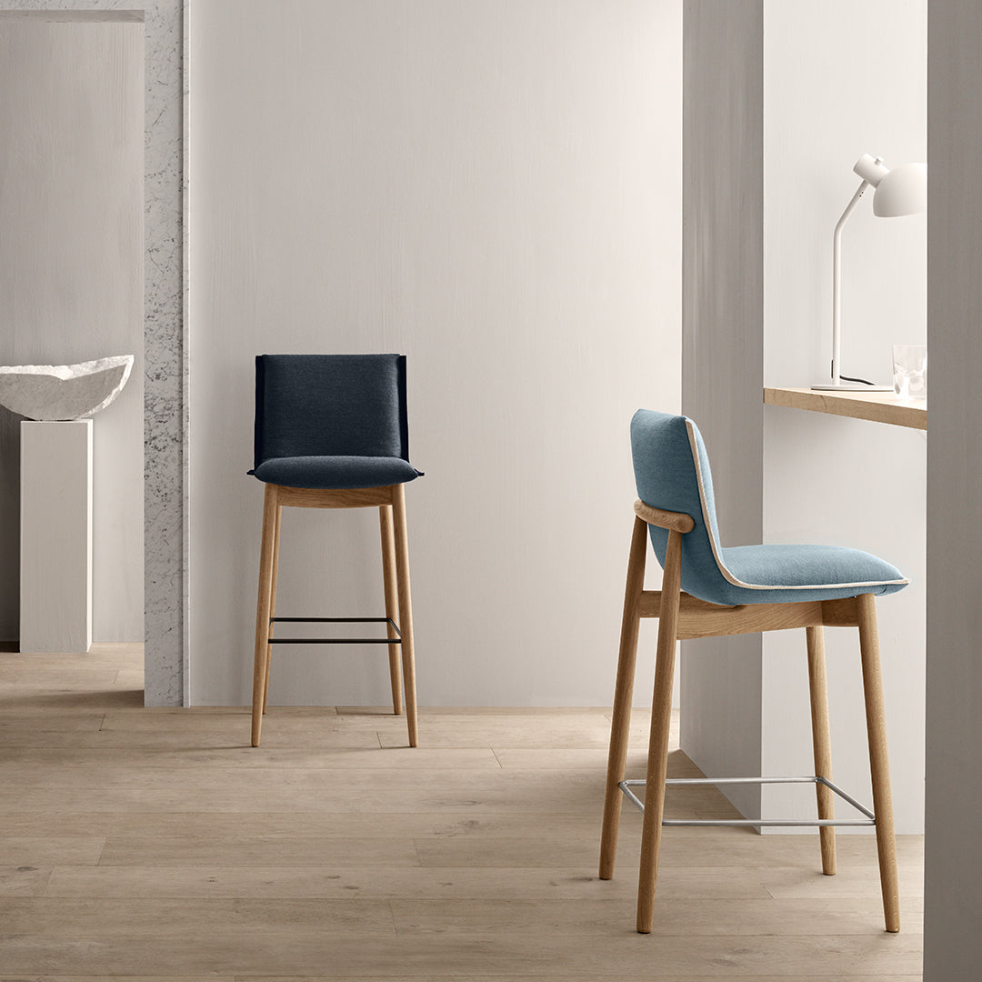 Modern bar stools in navy and light blue upholstery with natural wood legs, set against a minimalistic backdrop.