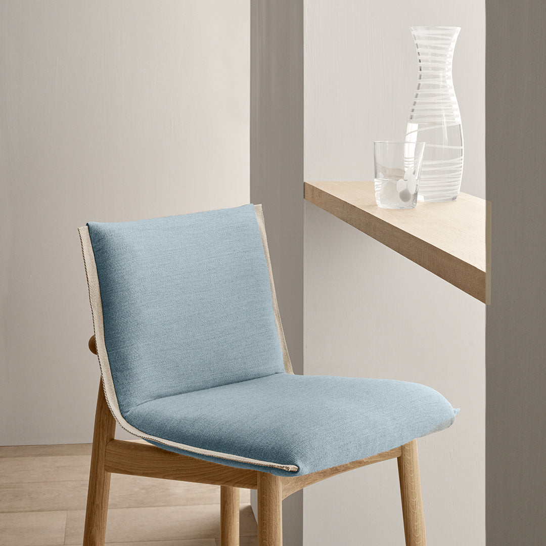 Light blue upholstered chair with a minimalist design, featuring a subtle texture and natural wood frame.