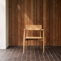 Light wood chair against a warm, textured wooden wall and a dark tile floor, creating a minimalist aesthetic.