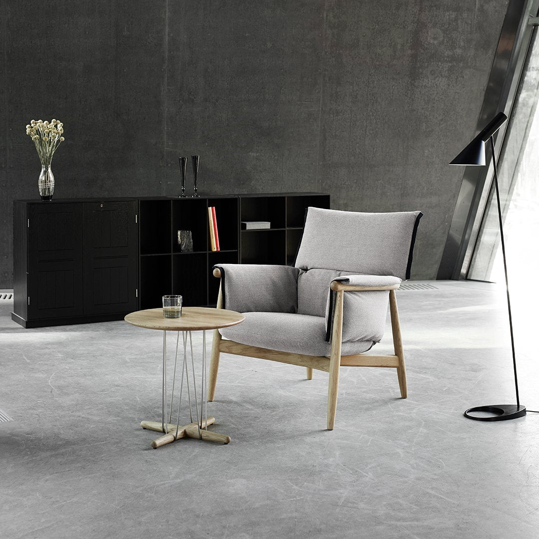 Light gray upholstered chair with natural wood legs, paired with a minimalistic wood table and sleek black accents.