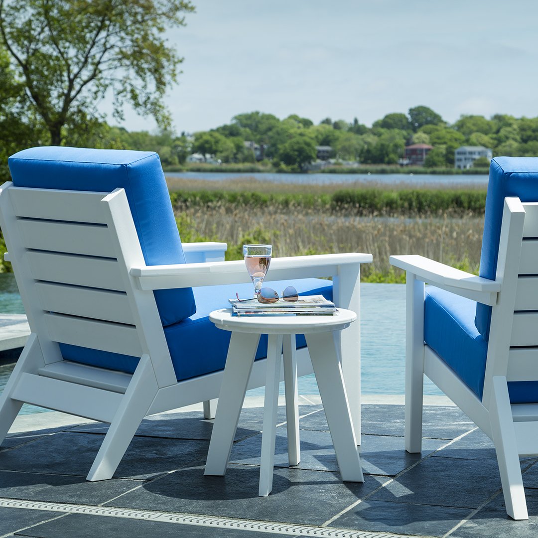 White outdoor chairs with striking blue cushions, complemented by a white side table against a serene outdoor backdrop.
