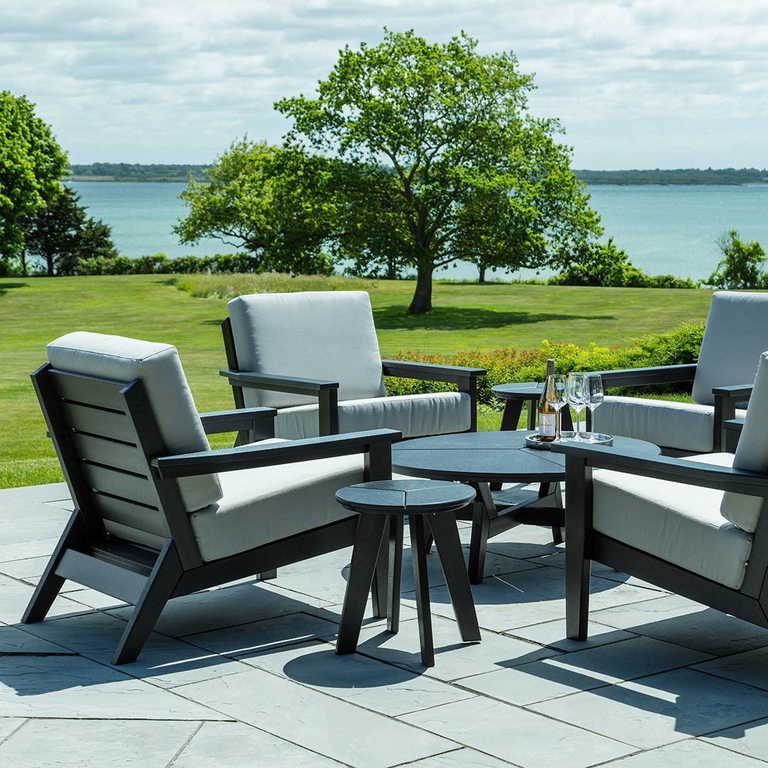 Stylish outdoor seating set in gray and black with sleek cushions, set against a lush green landscape and blue water.