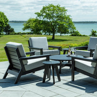 Stylish outdoor seating set in gray and black with sleek cushions, set against a lush green landscape and blue water.