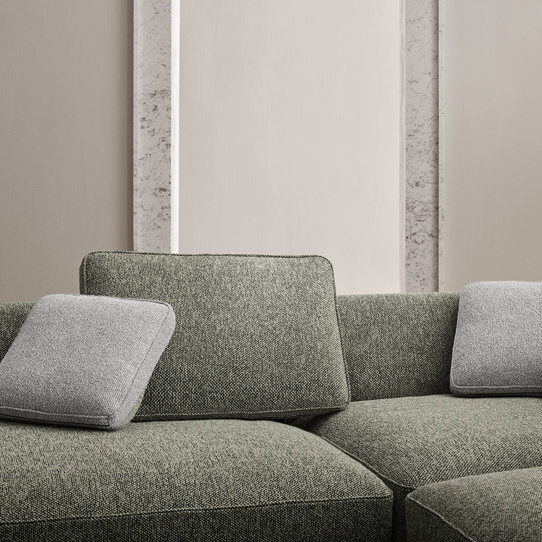 Textured green fabric sofa with two light gray pillows against a neutral wall, creating a modern and cozy aesthetic.