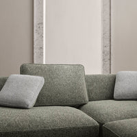 Textured green fabric sofa with two light gray pillows against a neutral wall, creating a modern and cozy aesthetic.