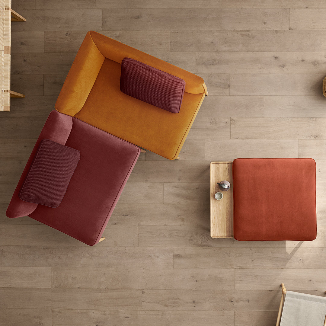 Two modern armchairs in mustard yellow and deep burgundy, paired with a rust-colored accent table on a light wood floor.