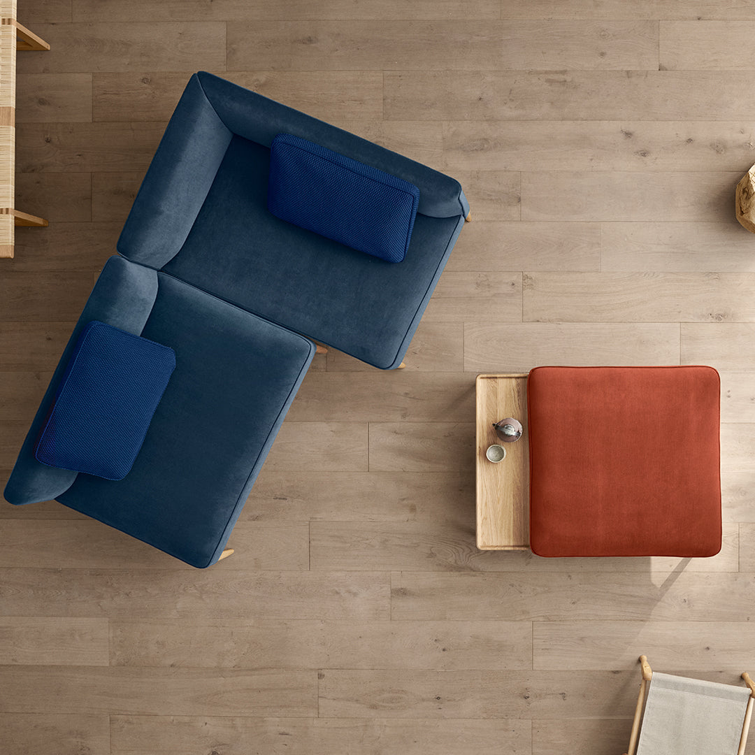 Blue and teal plush sectional sofa with navy accent pillows and a rust-colored ottoman on a light wood floor.
