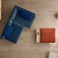 Blue and teal plush sectional sofa with navy accent pillows and a rust-colored ottoman on a light wood floor.