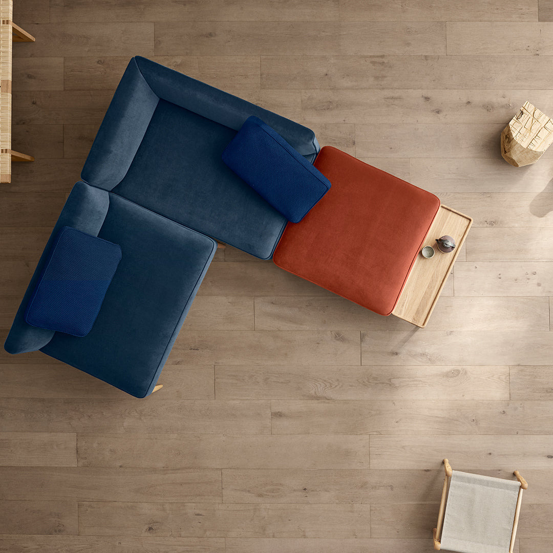 L-shaped sofa in deep blue and warm orange velvet with matching cushions on a light wood floor. Stylish and contemporary design.