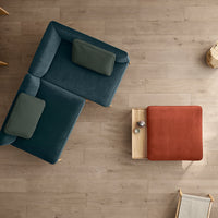 Teal and muted green upholstered sofa with a rust-colored ottoman on a light wood floor. Modern minimalist design.