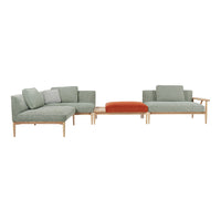 Modern sectional sofa in muted green fabric and light wood, featuring an accent pillow and an orange ottoman.