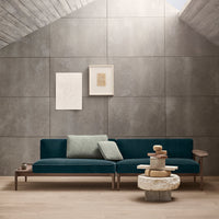 Teal sofa with textured gray cushions against a concrete-style wall, featuring clean lines and modern aesthetics.