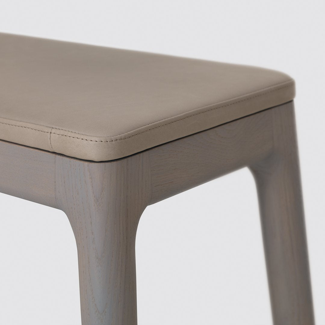 Beige leather top with smooth gray wooden legs, minimalist design. Perfect for modern decor.
