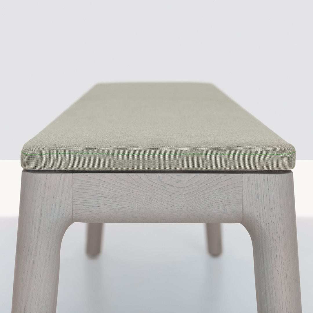 Light green upholstered bench with subtle stitching on a natural wood base. Modern and minimalist design.