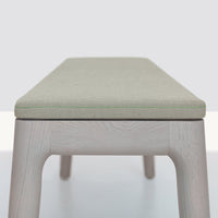 Light green upholstered bench with subtle stitching on a natural wood base. Modern and minimalist design.