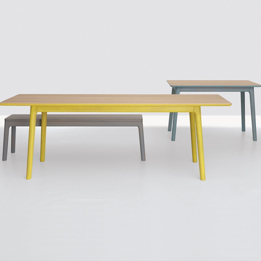 Three modern tables featuring a light wood top with yellow, gray, and blue legs on a minimalist white background.