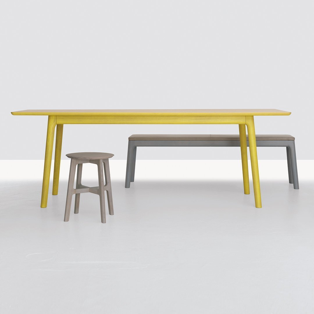 Yellow wooden table with gray bench and stool, featuring smooth finishes and clean lines on a white background.