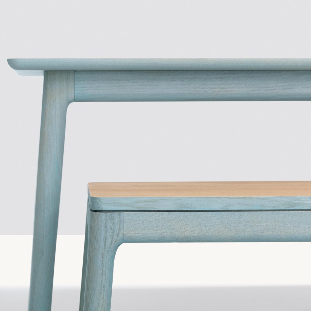 Light blue wooden table with subtle grain patterns and a contrasting light wood top. Modern and minimalist design.