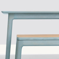 Light blue wooden table with subtle grain patterns and a contrasting light wood top. Modern and minimalist design.