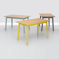 Three modern tables featuring natural wood tops with mint, yellow, and gray legs against a minimalist backdrop.